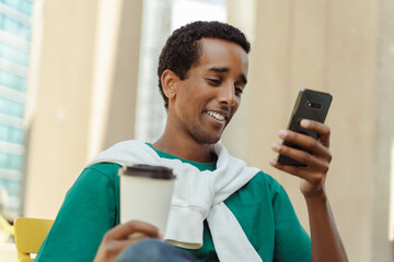 Portrait of smiling positive African American man sitting in cafe holding mobile phone