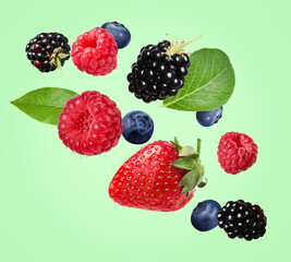 Many different fresh berries falling on light green background