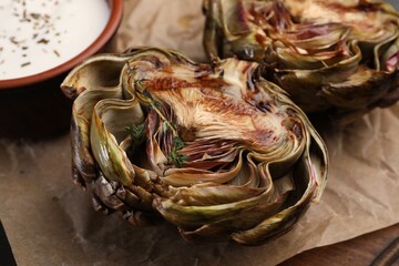 Tasty grilled artichoke and sauce on table, closeup