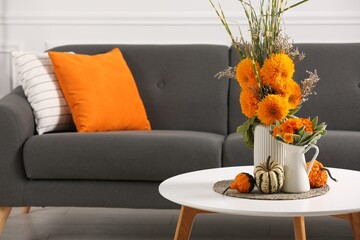 Beautiful autumn bouquets and pumpkins on coffee table near sofa in room