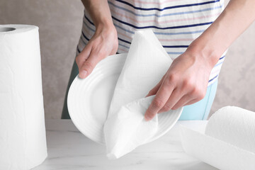 Obraz premium Woman wiping plate with tissue paper at white marble table, closeup