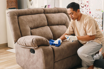 Man cleaning leather sofa at home with microfiber cloths and spray.
