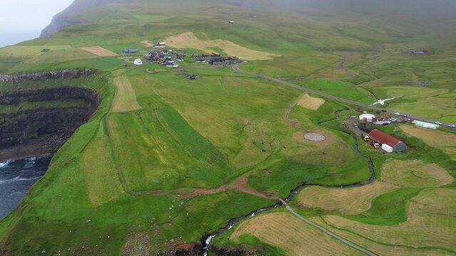 Aerial shot of a seagull flying over Gasadalur village and its farmlands near Mulafossur waterfall
