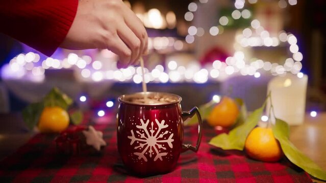 Mixing hot water and marshmallows in red glossy holiday mug close up. Winter traditional drinks. Christmas holidays and new year time 2024. Cooking hot chocolate drink close up view, hot cocoa recipe