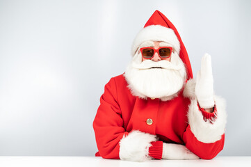 Portrait of santa claus sitting at a white table and pulling his hand up. 