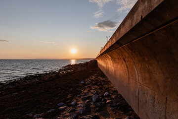 vue sur un brise vague en ciment au bord d'une plage rocailleuse en bord de mer lors d'un coucher...