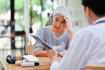 A stressed Asian retired old lady is being diagnosed and consulting treatment plans with a doctor.