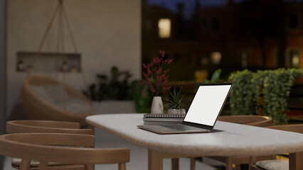 A white screen laptop mockup on a table on a home or apartment balcony at night.