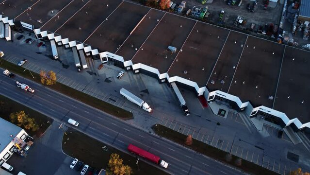 Semi-truck backing up towards warehouse loading dock. Drone view.