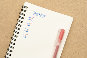 Top view of notebook with handwritten Checklist text and red pen. Checklist concept, checklist box...
