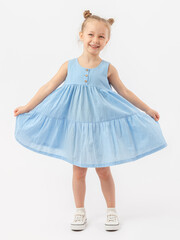 Carefree, fun. A 5-year-old girl with a fashionable hairstyle is spinning in a blue summer dress and sneakers on a white background and smiling.