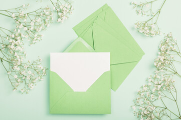 Delicate white gypsophila flowers, a green envelope and a blank card on a green background. Flat...