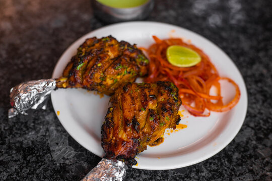 Tandoori chicken is a chicken dish prepared by roasting chicken marinated in yoghurt and spices in a tandoor or a clay oven, served with onion and green chutney