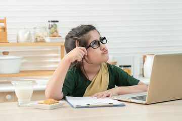 Smart little Pakistani girl wear eyeglasses online learning class, studying with teacher using laptop in kitchen, enjoying online education, thinking, Homeschooling, Distance Learning
