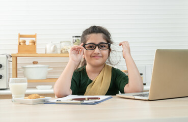 Happy cute little Asian girl wear eyeglasses online learning class, studying with teacher using laptop in kitchen, enjoying online education. Homeschooling, Distance Learning