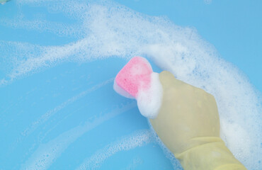 Fototapeta premium Human hand in protective glove with pink sponge in foam on blue background. 