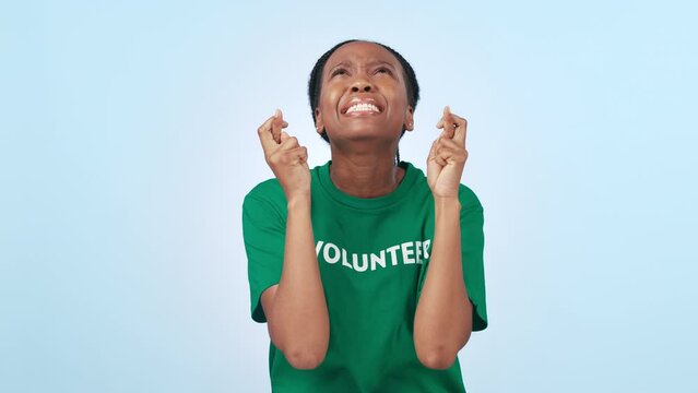 Hope, stress and black woman with fingers crossed, volunteer and donation on a blue studio background. African person, girl and charity worker with hand gesture, climate change and prayer with help