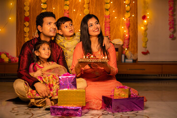 Happy young Indian family in traditional dress with lots of gifts around sitting on floor...