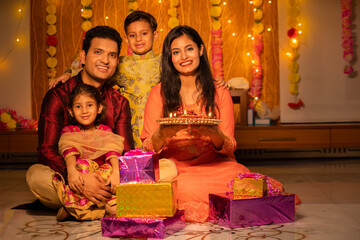 Portrait of happy young Indian family in traditional dress with lots of gifts around sitting on...