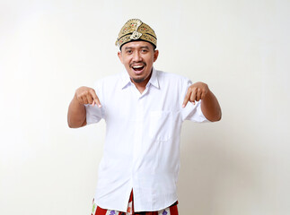 Asian man in balinese traditional costume standing while pointing down. Isolated on white background