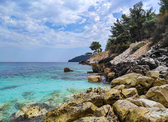 Landscape at Marble Beach or Saliara Beach , on Thassos Island in Greece , Europe , clear turquoise water , rocks falling into water and pine forest against a cloudy summer sky