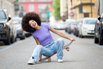 Happy young black woman sitting on skateboard - obrazy, fototapety, plakaty