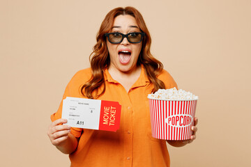 Young fun surprised shocked chubby overweight woman in 3d glasses wear orange shirt casual clothes watch movie film hold ticket bucket of popcorn in cinema isolated on plain beige background studio.