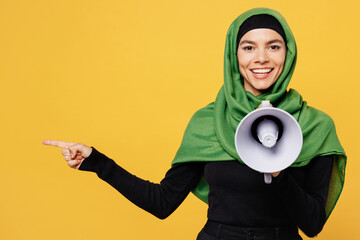 Young arabian asian muslim woman wear green hijab abaya black clothes scream in megaphone announce...