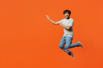 Fototapeta na wymiar Full body young fun smiling happy Indian man he wears t-shirt casual clothes jump high look camera point index finger aside isolated on orange red color background studio portrait. Lifestyle concept.