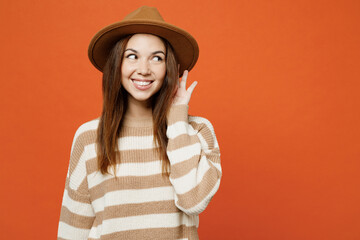 Young curious nosy woman she wear striped sweater hat casual clothes try to hear you overhear listening intently isolated on plain orange red color wall background studio portrait. Lifestyle concept.
