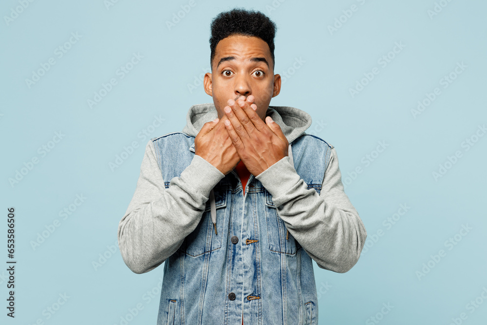 Wall mural Young sad man of African American ethnicity wear denim jacket orange t-shirt cover mouth with hand look camera isolated on plain pastel light blue cyan background studio portrait. Lifestyle concept. - Wall murals