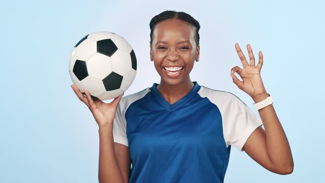 Face, soccer and ok sign with sports, black woman and fitness on blue studio background. Portrait, African person or football player with happiness, promotion or agreement with perfect, icon or smile