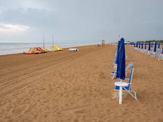 Closed beach parasol at empty seaside coast. Beach in Italy - 653587333