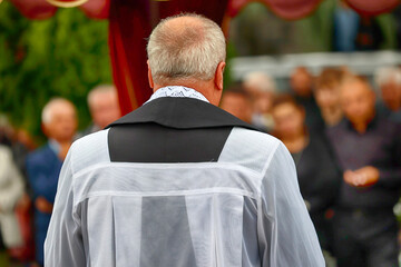 Ksiądz katolicki w komży z fioletowa stułą podczas celebracji pogrzebu. Obrzęd. 