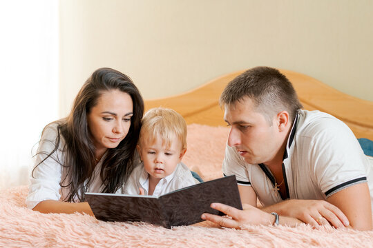 happy family lying on the bed reading a book, mom dad and little son