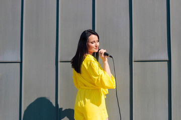Woman vocalist with dark hair in a dress sings into a microphone