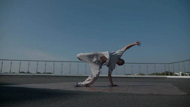 The guy coolly dances breakdance on the roof of the house. Slow motion shooting. A man dances an energetic athletic dance.