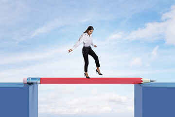 Attractive young european female crossing pencil bridge on sky background. Career problem and gap concept.