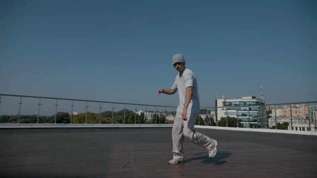 The guy coolly dances breakdance on the roof of the house. Slow motion shooting. A man dances an energetic athletic dance.