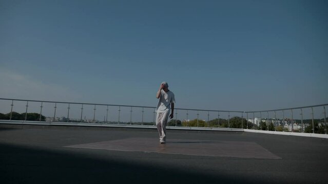 The guy coolly dances breakdance on the roof of the house. Slow motion shooting. A man dances an energetic athletic dance.