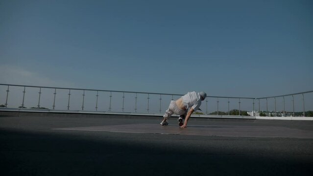 The guy coolly dances breakdance on the roof of the house. Slow motion shooting. A man dances an energetic athletic dance.