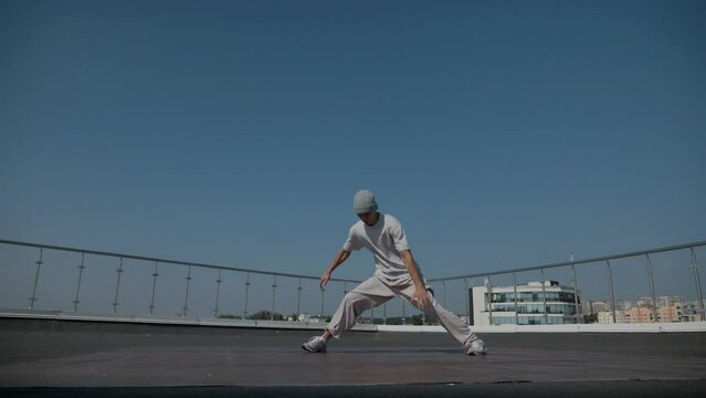 The guy coolly dances breakdance on the roof of the house. Slow motion shooting. A man dances an energetic athletic dance.