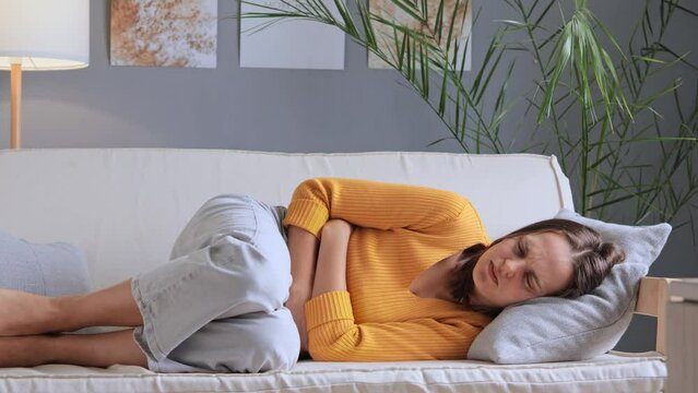 Unhappy woman suffering from stomachache after eating spoiled food feels discomfort in belly has disorder has appendicitis symptoms period ache lies on couch at home.