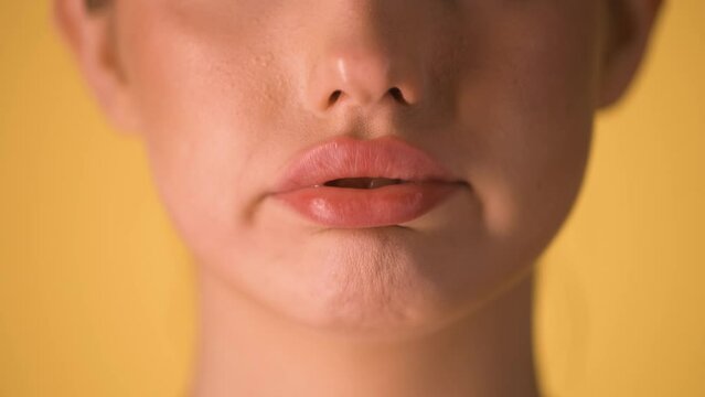Extreme close up of beautiful woman lips while she makes her lips flutter because something is exhausting or impossible in front of yellow background in slow motion