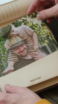 Vertical video. Hands inserting printed photos into family picture album. Father day concept.