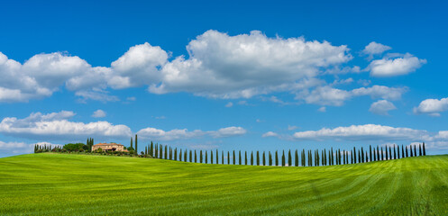Obraz premium Beautiful Tuscan landscape with traditional farmhouse and dramatic clouds on a sunny day in Val d'Orcia, Italy