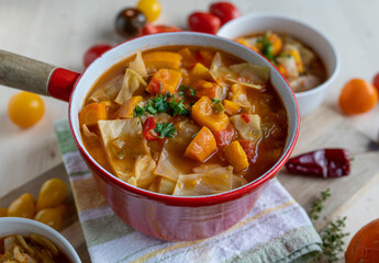 Pumpkin soup with cabbage, carrots and tomatoes in a red pot