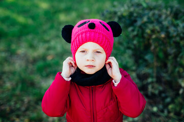 children dressed in a hat against a background of green bushes in autumn. the onset of cold weather, warm clothes, happy children. bright clothes