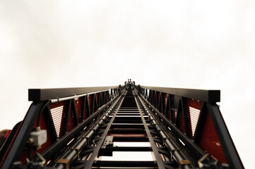 Tall extendable fire ladder close up in perspective on cloud sky background.in the distance, fire escape maintenance, 911 fire truck © Vadym