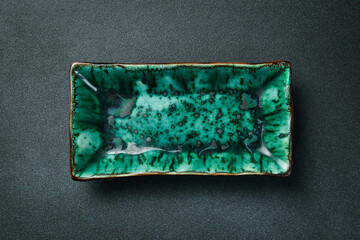 Green creative rectangular plate for serving food. On a black stone background. Free space for text.